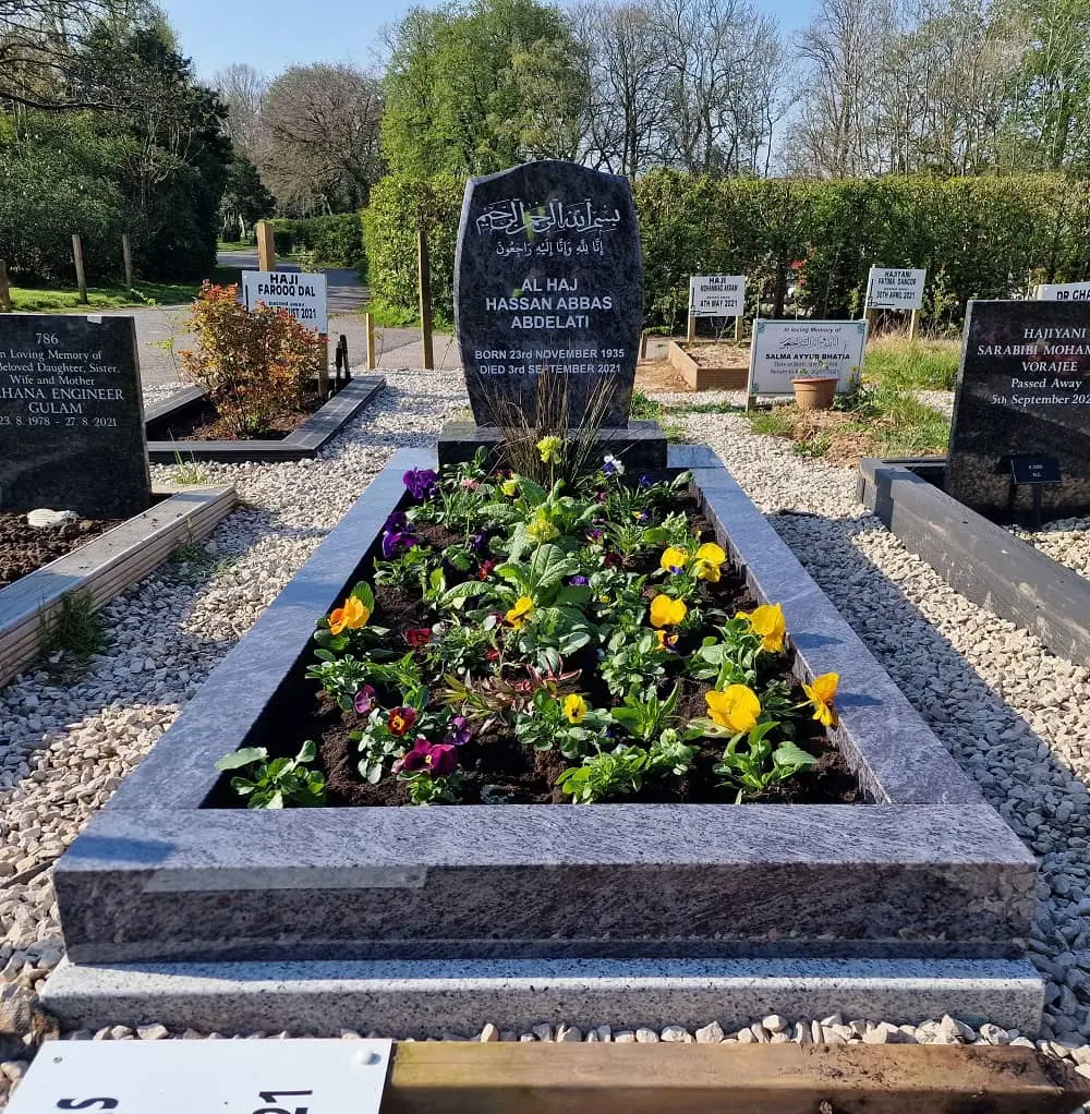 Shaped grey memorial with an engraved inscription and colourful flowers inside the kerb
