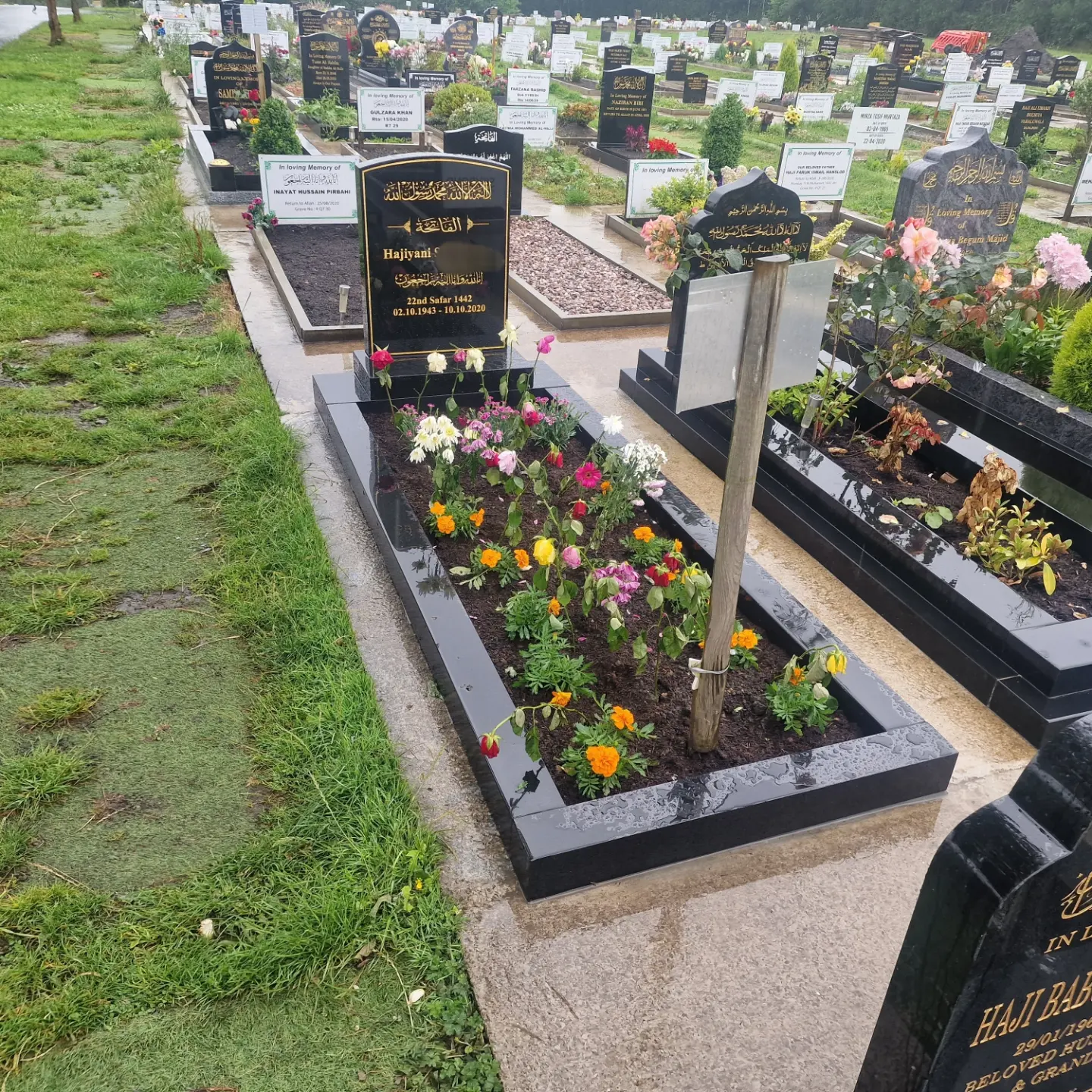 Black arched headstone with gold lettering and a matching kerb filled with flowers
